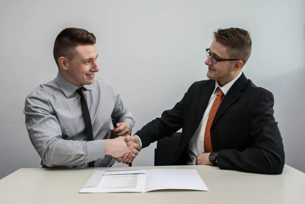 Two business professionals shaking hands after signing a contract, symbolizing agreement and compliance with ISO 45001 certification standards.
