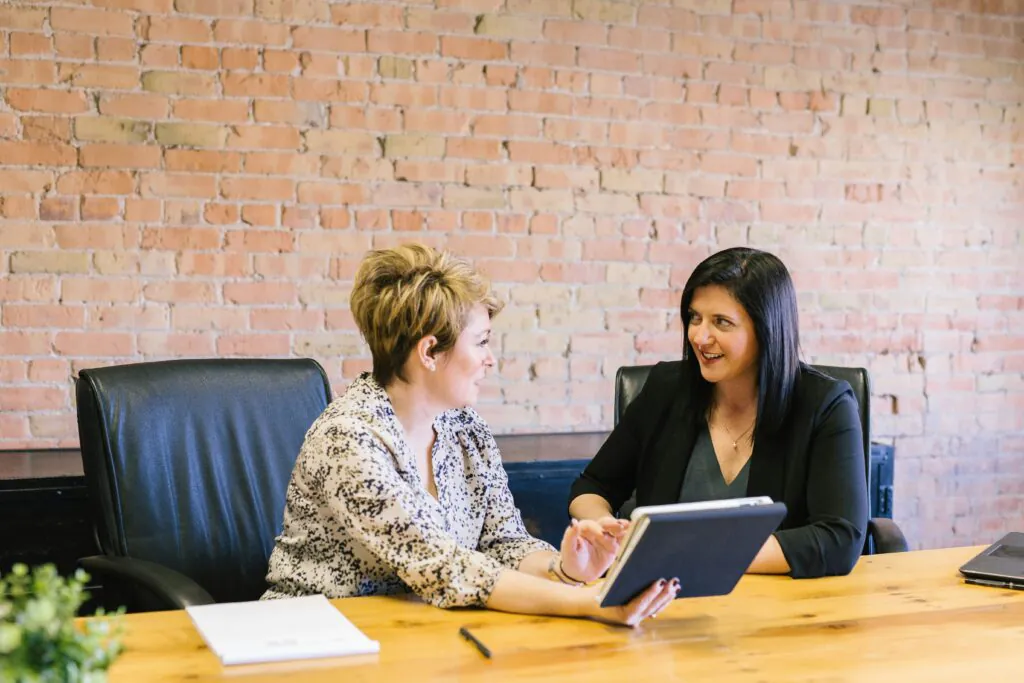 Two female professionals discussing information on a digital tablet in a meeting.
