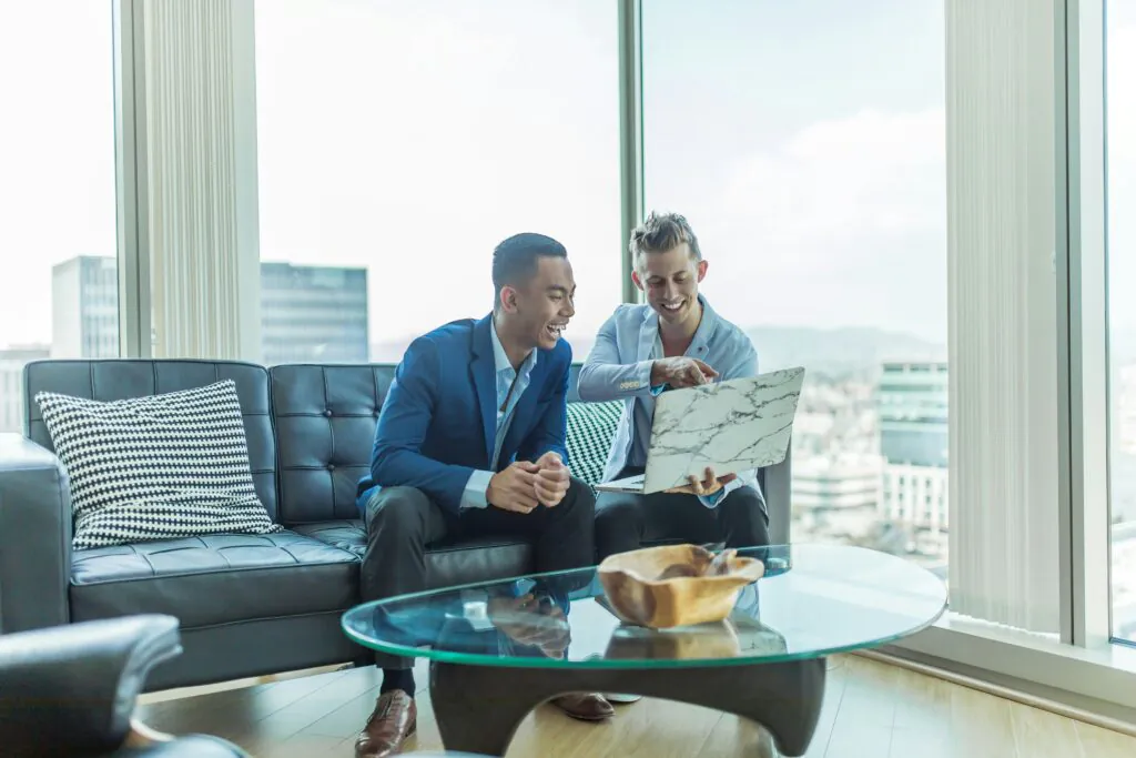 Two smiling businessmen look at a laptop, successfully reviewing their company's GDPR compliance status.