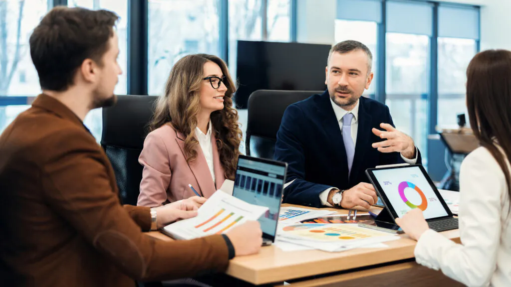 Three professionals engaged in a discussion during a meeting with laptops and documents
