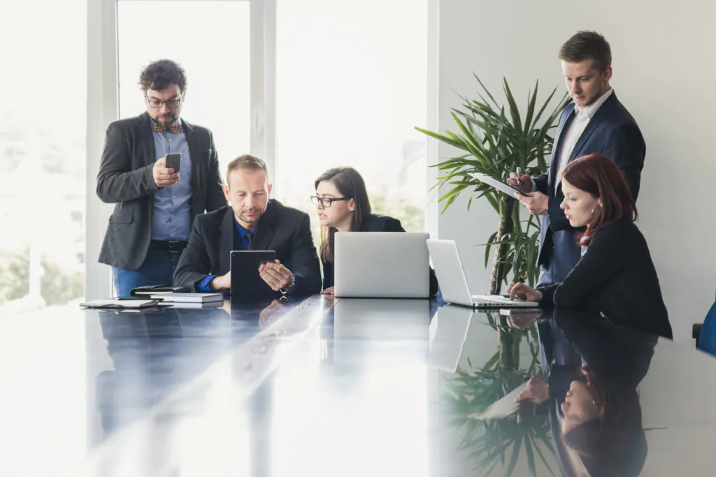 A team of five business professionals meeting around a large table, collaborating on a distribution logistics or GDP audit plan.