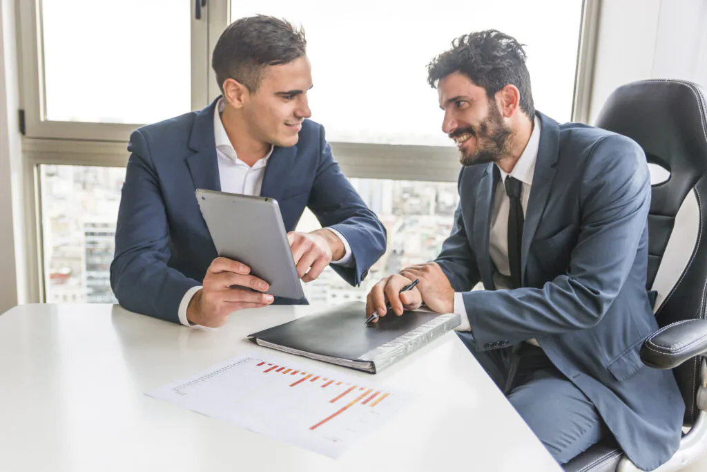 Two asset managers in a meeting, one showing successful performance metrics on a tablet, demonstrating the positive results of an ISO 55001 implementation