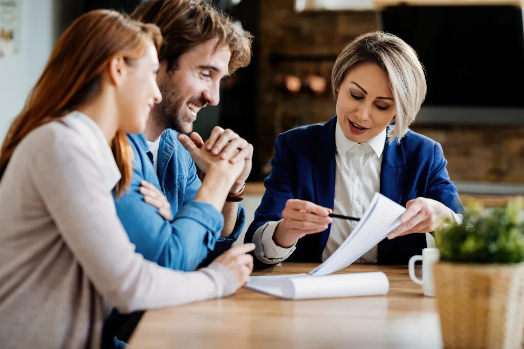 A female HIPAA compliance consultant reviews documents with a smiling couple at a table, explaining the process for achieving HIPAA certification for their practice