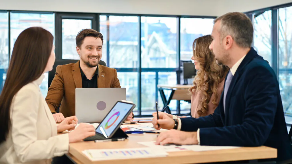 Four team members discussing a data-driven facility management strategy, with a tablet in the foreground displaying a pie chart to support evidence-based decision-making as mandated by ISO 41001 requirements.