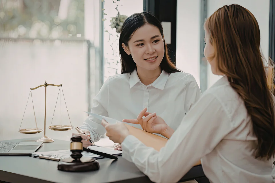 A female professional in a white shirt discusses a document with a client in an office featuring a gavel and scales of justice. This represents the legal framework, regulatory compliance, and official certification standards required for GLP.